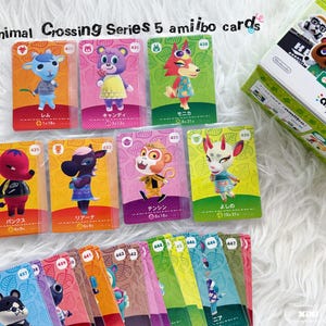 May include: A collection of Animal Crossing Series 5 amiibo cards featuring various characters, with a box of amiibo cards in the background. The cards have colorful designs and Japanese text. The text "Animal Crossing Series 5 amiibo cards" is at the top.