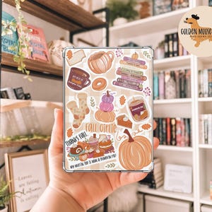 May include: A clear phone case decorated with autumn-themed stickers. The stickers depict a pumpkin, coffee mug, donuts, and the text "Fall Girlie". The case has a beige and white checkered background. The Golden Moose Studio logo is visible.