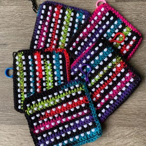 Könnte beinhalten: Eine Sammlung farbenfroher, quadratischer Häkeltaschen mit weißen Perlenakzenten. Jede Tasche hat ein anderes Farbschema, darunter Pink, Lila, Grün und Blau, und ist mit einem passenden Verschluss versehen.