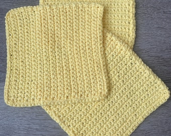 May include: Three yellow crocheted dishcloths stacked on top of each other. The dishcloths are made with a simple stitch pattern and have a soft, absorbent texture.