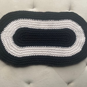 May include: A black and white oval crochet rug with a white border. The rug is made of thick yarn and has a textured surface.