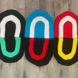 May include: Three crocheted oval-shaped floor mats with a black base and a white stripe. The top half of each mat is a different color: green, blue, and red. The bottom half of each mat is a different color: green, red, and yellow.