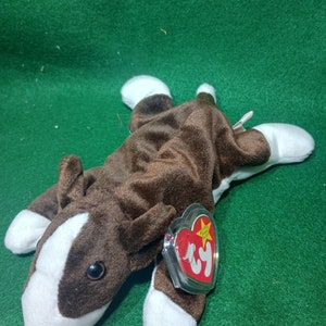 May include: Brown and white Ty Beanie Baby dog plush toy with a white tag that says "Ty Beanie Babies" and "Ty".