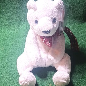 May include: White plush polar bear wearing a red and white patterned scarf. The bear is sitting with its paws tucked in front of it.