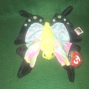 May include: A colorful butterfly plush toy with black wings and a yellow body. The toy has a Ty Beanie Baby tag attached.