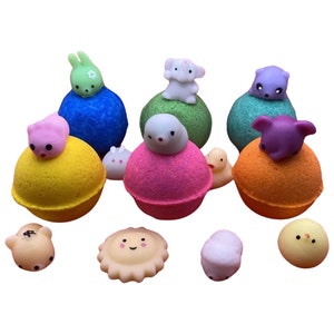 May include: Assortment of colorful bath bombs with cute animal and character figurines on top. The bath bombs are in various colors, including yellow, blue, green, orange, and pink. The figurines are made of a soft, squishy material and are in various colors and designs.