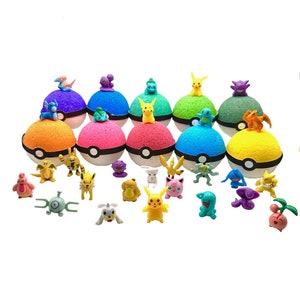 May include: A set of 12 colorful bath bombs shaped like Poke Balls, each with a different Pokemon character on top. The bath bombs are arranged in a semi-circle, with the Pokemon characters facing outwards. There are also 18 small plastic Pokemon figures scattered in front of the bath bombs.