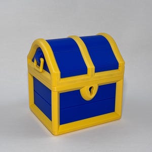 Puede incluir: Un pequeño cofre del tesoro de juguete, con una combinación de colores vibrantes. El cofre es azul con detalles amarillos, incluyendo el asa y los bordes. Tiene una cerradura y una tapa con bisagras.