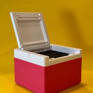 May include: A small, white and pink box with a hinged lid. The lid is open and reveals a black interior.
