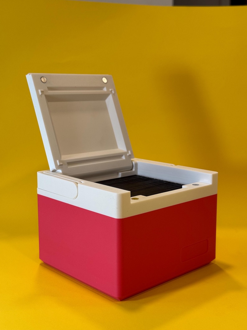 May include: A small, white and pink box with a hinged lid. The lid is open and reveals a black interior.