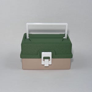 May include: A two-tone, small tackle box with a white handle and latch. The top is a textured, dark green, and the bottom is a light tan color. The handle and latch are white.