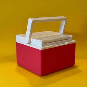 May include: A small, red and white cooler with a white handle. The cooler is closed and has a white lid.
