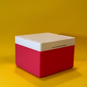May include: A small, square, red and white storage box with a hinged lid. The box is made of plastic and has a smooth, matte finish.
