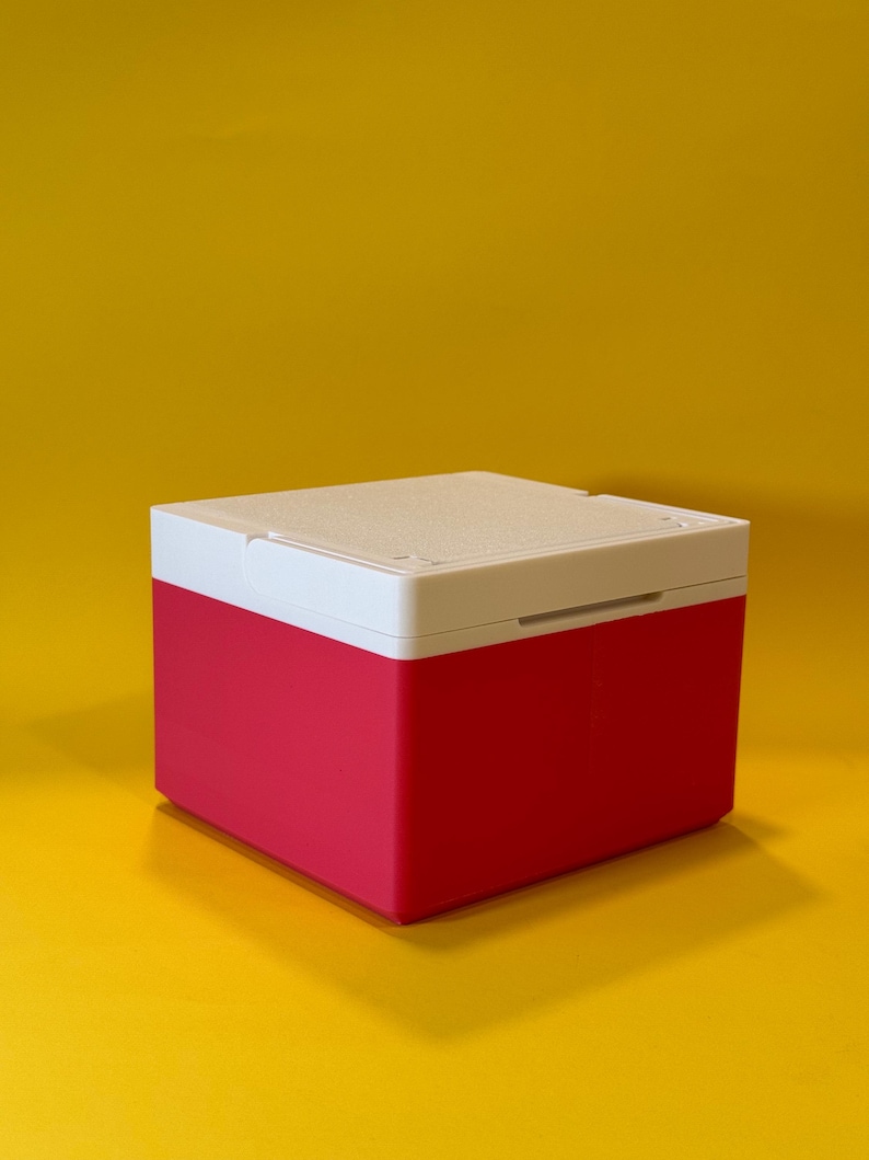 May include: A small, square, red and white storage box with a hinged lid. The box is made of plastic and has a smooth, matte finish.