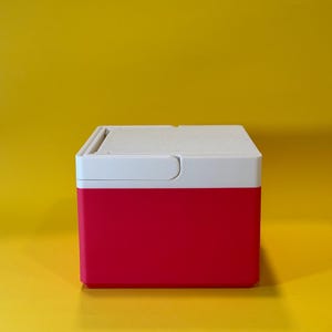 May include: A small, red and white cooler with a hinged lid. The cooler is made of plastic and has a smooth, glossy finish.