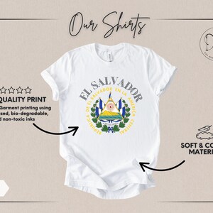 May include: A white short-sleeved t-shirt featuring the coat of arms of El Salvador printed in the center. The design includes the text EL SALVADOR and REPUBLICA DE EL SALVADOR EN LA AMERICA CENTRAL. The shirt is displayed with informational text.