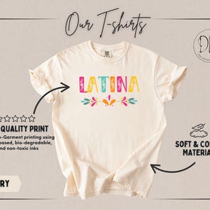 Puede incluir: Camiseta de color marfil con la palabra "LATINA" en letras de colores. La camiseta presenta un dise&ntilde;o floral debajo de la palabra y el texto "Our T-shirts". La camiseta est&aacute; hecha de un material suave y c&oacute;modo.