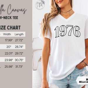 May include: White Bella Canvas V-neck tee with the year "1976" printed in black. The image includes a size chart with measurements in inches. The shirt is worn by a person in blue jeans.