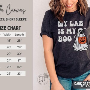 May include: A dark grey heather short-sleeve crewneck t-shirt featuring a graphic of a dog dressed as a ghost holding an orange jack-o'-lantern bucket with the text 'MY LAB IS MY BOO'. A size chart with width and length in inches is visible.