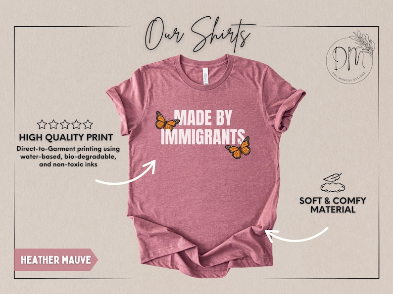 Pu&ograve; includere: Una t-shirt color malva m&eacute;lange con la scritta bianca MADE BY IMMIGRANTS centrata sul petto. Due farfalle monarca arancioni e nere sono posizionate vicino al testo, una a sinistra della parola MADE e una a destra di IMMIGRANTS.