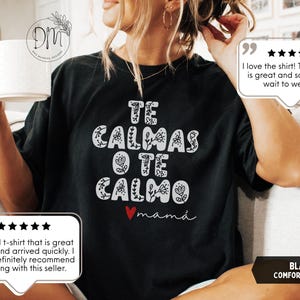 May include: Black comfort colors t-shirt with the text "TE CALMAS O TE CALMO mam&aacute;" in white, floral-style lettering. A red heart is below the text. The shirt has a relaxed fit.