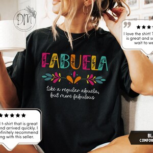 May include: Black comfort colors t-shirt with the word "FABUELA" in colorful letters. The shirt also has the phrase "like a regular abuela, but more fabulous" in white text. The shirt is a comfortable fit.