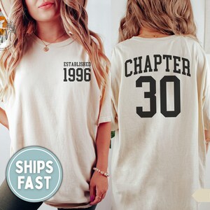 May include: Ivory-colored t-shirt with the text "ESTABLISHED 1996" on the front and "CHAPTER 30" on the back. The shirt has a relaxed fit and short sleeves. The text is in a bold, black font. The shirt is a casual style.
