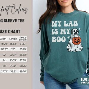 May include: A blue spruce long-sleeve t-shirt featuring a graphic of a Labrador retriever dressed as a ghost holding a jack-o'-lantern bucket with the text MY LAB IS MY BOO. A size chart is visible on the left with measurements in inches.