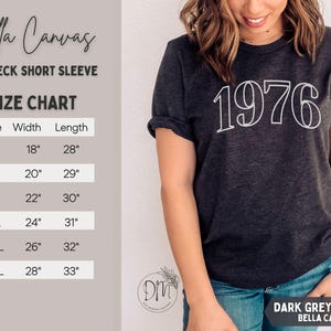May include: Dark grey heather Bella Canvas crewneck short sleeve t-shirt with the year "1976" in white. The size chart shows measurements in inches: S (18" width, 28" length), M (20" width, 29" length), L (22" width, 30" length), XL (24" width, 31" length), 2XL (26" width, 32" length), 3XL (28" width, 33" length).
