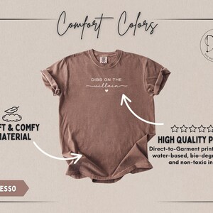 May include: Espresso-colored t-shirt with the text "DIBS ON THE villain" in white script. The shirt features a crew neck and rolled sleeves. The image also highlights the soft and comfy material and high-quality print.