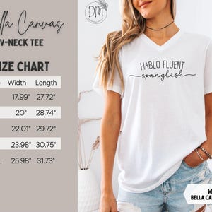 K&ouml;nnte beinhalten: Wei&szlig;es Bella Canvas V-Ausschnitt-T-Shirt mit dem Text "HABLO FLUENT spanglish" in schwarzer Schrift. Gr&ouml;&szlig;entabelle zeigt Ma&szlig;e in cm. Das Shirt ist ein Freizeitkleidungsst&uuml;ck.