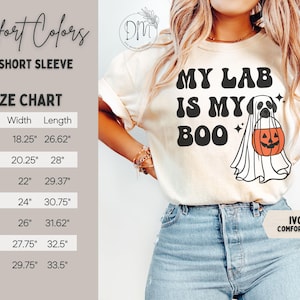 May include: An ivory short-sleeve t-shirt featuring the black text MY LAB IS MY BOO and a graphic of a dog wearing a ghost costume and holding an orange jack-o'-lantern. A size chart displays width and length measurements in inches for sizes S to 4XL.