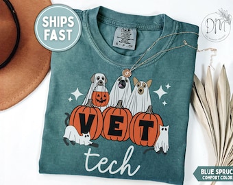 Peut inclure: Un t-shirt bleu épicéa Comfort Colors avec un motif de trois chiens déguisés en fantômes derrière trois citrouilles orange. Les citrouilles portent les lettres V, E et T, et le mot tech est imprimé en dessous en écriture blanche.