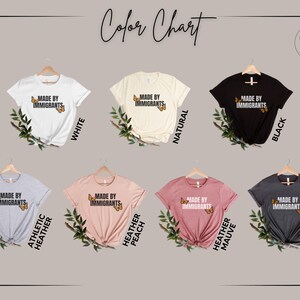 Pu&ograve; includere: Una tabella colori con sette magliette a maniche corte in bianco, naturale, nero, grigio melange, pesca melange, malva melange e grigio scuro melange. Ogni maglietta mostra il testo MADE BY IMMIGRANTS con due grafiche di farfalle arancioni.