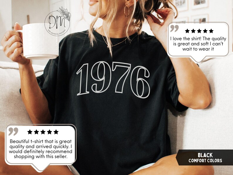 May include: Black t-shirt with the year "1976" in white, outlined font. The shirt is part of the "Comfort Colors" collection. The image also includes customer reviews.