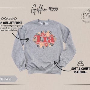 May include: Sport grey sweatshirt with the word "Tia" in red, surrounded by a floral design. The sweatshirt is made of soft and comfy material. The image also includes text that says "High Quality Print" and "Direct-to-Garment printing using water-based, bio-degradable, and non-toxic inks."