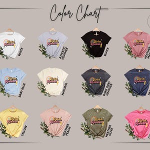 May include: A color chart displaying twelve short-sleeve t-shirts in various colors including white, athletic heather, black, heather mauve, baby blue, natural, dark grey heather, heather navy, yellow, heather peach, heather olive, and charity pink.