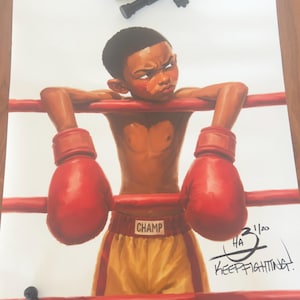 May include: A print featuring a young boxer in yellow shorts and red gloves leaning on red ring ropes, with the text "CHAMP" on the waistband and "KEEP FIGHTING!" signed by the artist. Three small black figurines are placed on the print.
