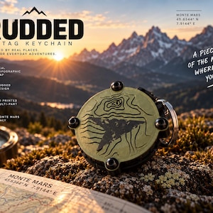 May include: A round, olive-green AirTag keychain featuring a black topographic map design of Monte Mars, Italy. The device has four black screws on its face and a metal ring attachment, presented with text including RUDDED AIRTAG KEYCHAIN.