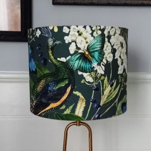May include: A dark green lampshade featuring a peacock and butterfly design. The lampshade has a white floral pattern and is made of fabric.