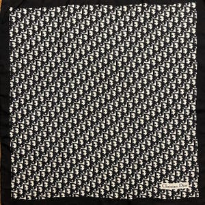 May include: Square black and white scarf with an all-over pattern of repeating black "CD" logos. The scarf has a black border and the words "Christian Dior" are printed in white on a small label in the bottom right corner.