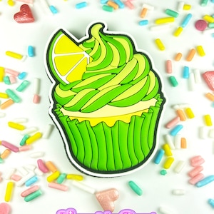 May include: Green and yellow cupcake with a lemon slice on top. The cupcake is surrounded by colorful sprinkles.