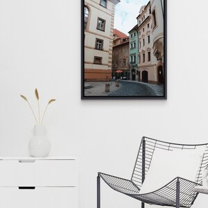 K&ouml;nnte beinhalten: Ein Foto einer engen Stra&szlig;e in Prag, Tschechien. Die Stra&szlig;e ist ges&auml;umt von bunten Geb&auml;uden, von denen einige verzierte Fassaden haben. Die Geb&auml;ude sind eine Mischung aus Gelb, Gr&uuml;n und Rosa. Die Stra&szlig;e ist leer, bis auf ein paar Menschen, die in der Ferne gehen.