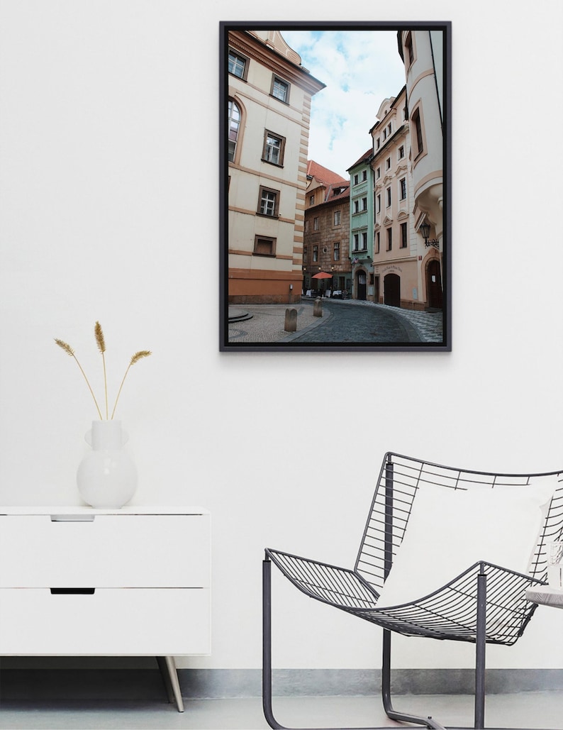 K&ouml;nnte beinhalten: Ein Foto einer engen Stra&szlig;e in Prag, Tschechien. Die Stra&szlig;e ist ges&auml;umt von bunten Geb&auml;uden, von denen einige verzierte Fassaden haben. Die Geb&auml;ude sind eine Mischung aus Gelb, Gr&uuml;n und Rosa. Die Stra&szlig;e ist leer, bis auf ein paar Menschen, die in der Ferne gehen.