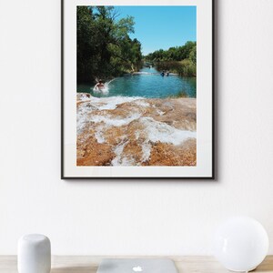 Może przedstawiać: Zdjęcie w ramie przedstawiające rzekę, w kt&oacute;rą skacze osoba. Rzeka jest otoczona drzewami, a woda ma jasnoniebieski kolor. Zdjęcie jest oprawione w czarną ramę.