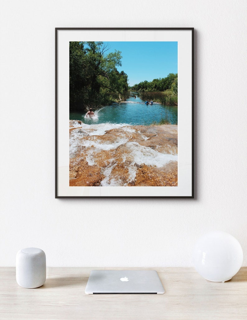 Może przedstawiać: Zdjęcie w ramie przedstawiające rzekę, w kt&oacute;rą skacze osoba. Rzeka jest otoczona drzewami, a woda ma jasnoniebieski kolor. Zdjęcie jest oprawione w czarną ramę.