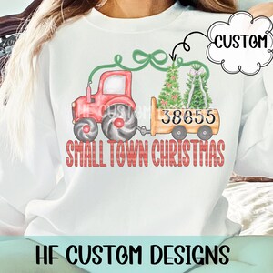 May include: White sweatshirt with a red tractor design pulling a wagon with Christmas trees. The wagon displays the number 38655. The text "SMALL TOWN CHRISTMAS" is printed below the tractor. A custom design.