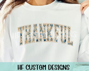 May include: White sweatshirt with the word "THANKFUL" printed in a brown and blue floral pattern.