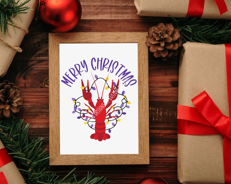 May include: A framed print with a red crawfish with purple and yellow lights wrapped around it. The text "Merry Christmas" is written in purple letters on a white background.