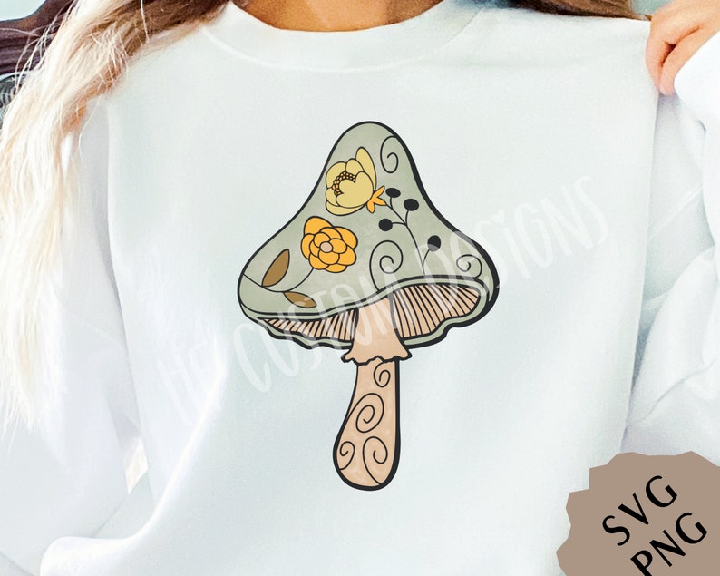 May include: A white sweatshirt with a green, yellow, and brown mushroom graphic with floral details. The mushroom has a stem with a swirl pattern.